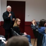 Mężczyzna stoi i mówi do mikrofonu. Uczestnicy konferencji słuchają.
