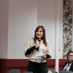 Kobieta stoi i mówi do mikrofonu podczas dyskusji po referatach.