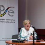 Kobieta wygłasza referat. W tle roll-up Polskiego Seminarium Etnomuzykologicznego.