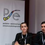 Kobieta i mężczyzna wygłaszają referat. W tle roll-up Polskiego Seminarium Etnomuzykologicznego.