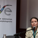 Kobieta wygłasza referat. W tle roll-up Polskiego Seminarium Etnomuzykologicznego.