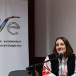 Kobieta wygłasza referat. W tle roll-up Polskiego Seminarium Etnomuzykologicznego.