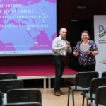 Dwie uśmiechnięte osoby. W tle ekran z plakatem konferencji.