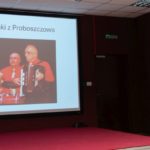 Kobieta wygłasza referat. Na ekranie wyświetlona prezentacja.