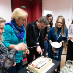 Grupa osób krojąca jubileuszowy tort.