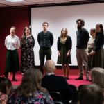Grupa kobiet i mężczyzn prezentuje śpiew podczas konferencji. Publiczność słucha.