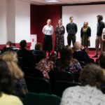 Grupa kobiet i mężczyzn prezentuje śpiew podczas konferencji. Publiczność słucha.