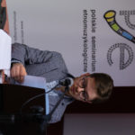 Prelegent czyta referat. W tle rollup Polskiego Seminarium Etnomuzykologicznego.