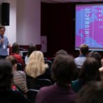 Mężczyzna mówi do mikrofonu. Uczestnicy konferencji słuchają