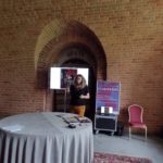 Kobieta wygłasza referat. Przed kobietą okrągły stół.