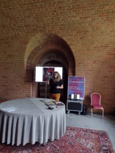 Kobieta wygłasza referat. Przed kobietą okrągły stół.