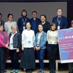 Grupa osób stoi. Mężczyzna trzyma oprawiony plakat konferencji.